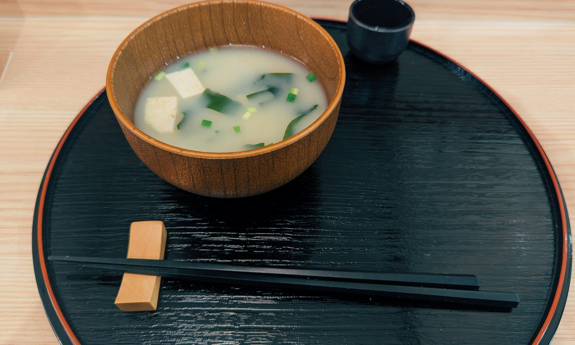 黒いお盆に乗った味噌汁と箸の写真