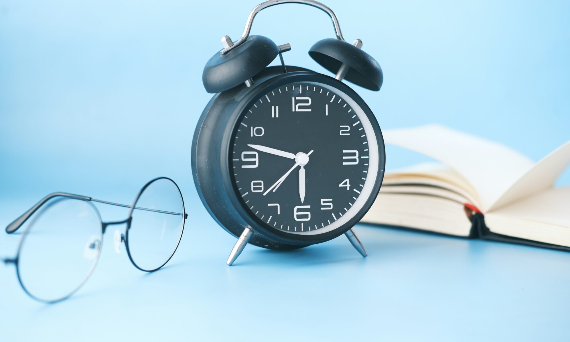 青い背景に開いた本と時計とメガネの写真